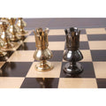 Gold and grey Victorian metal rooks standing side-by-side on a chessboard.
