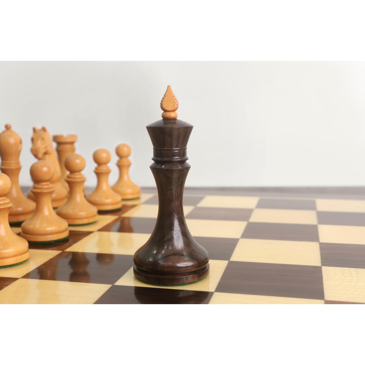 Close-up of the dark rosewood king from the Candidates Series minimalist chess set standing on a wooden chessboard.
