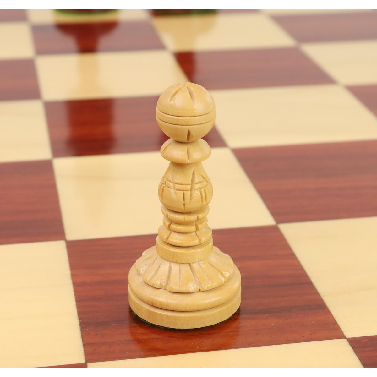 A single hand-carved Boxwood pawn from the Lotus Series resting on a wooden chess board.
