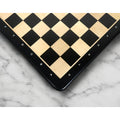 Ebony and maple wood chess board corner resting on an elegant white marble surface.