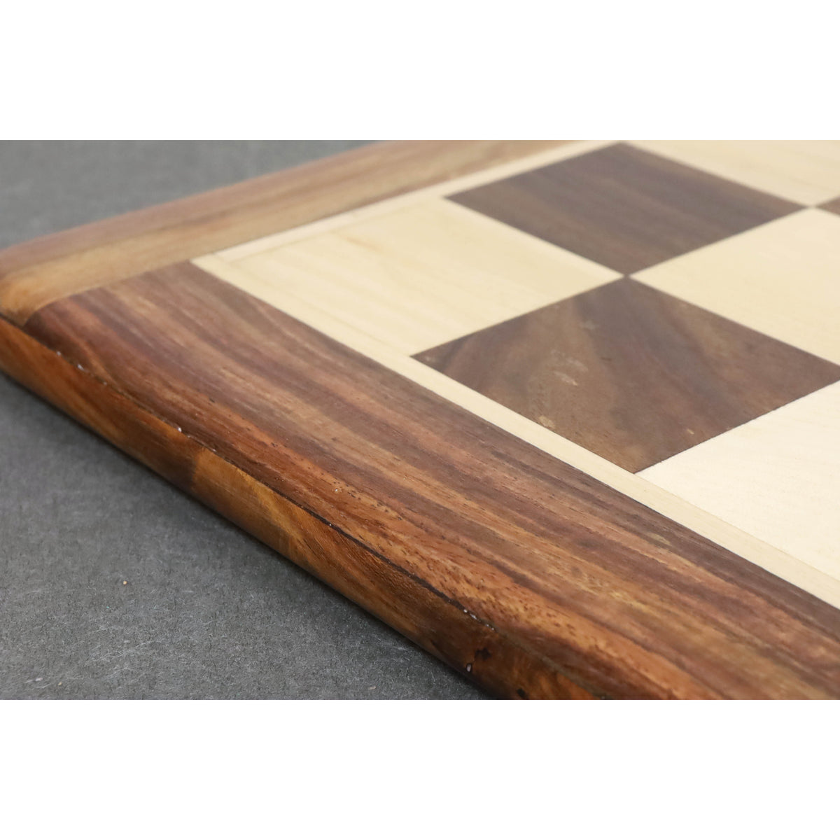 Detailed view of the artisanal joinery and smooth edges of a luxury rosewood and maple chess board.