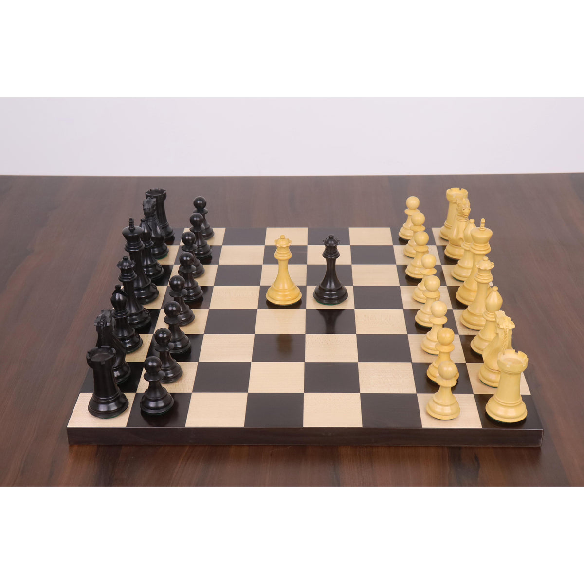 Sleek Staunton ebony and boxwood chess pieces set up in play on a wooden board.
