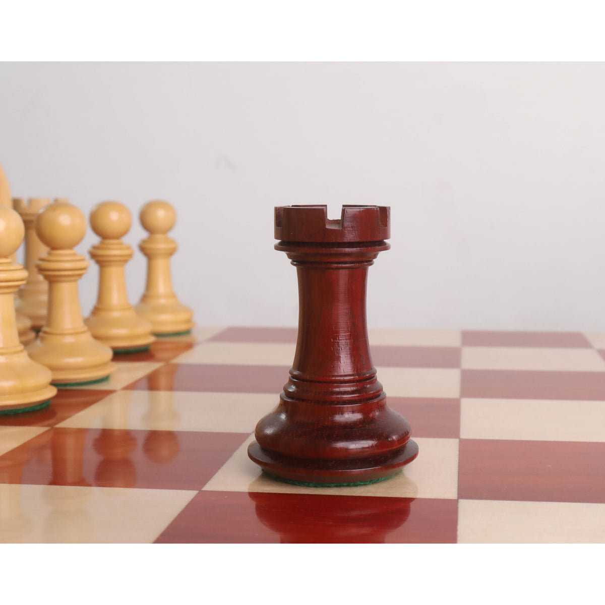 Bud Rosewood rook of a 4.6" Bath Luxury Staunton chess set standing on a wooden board.