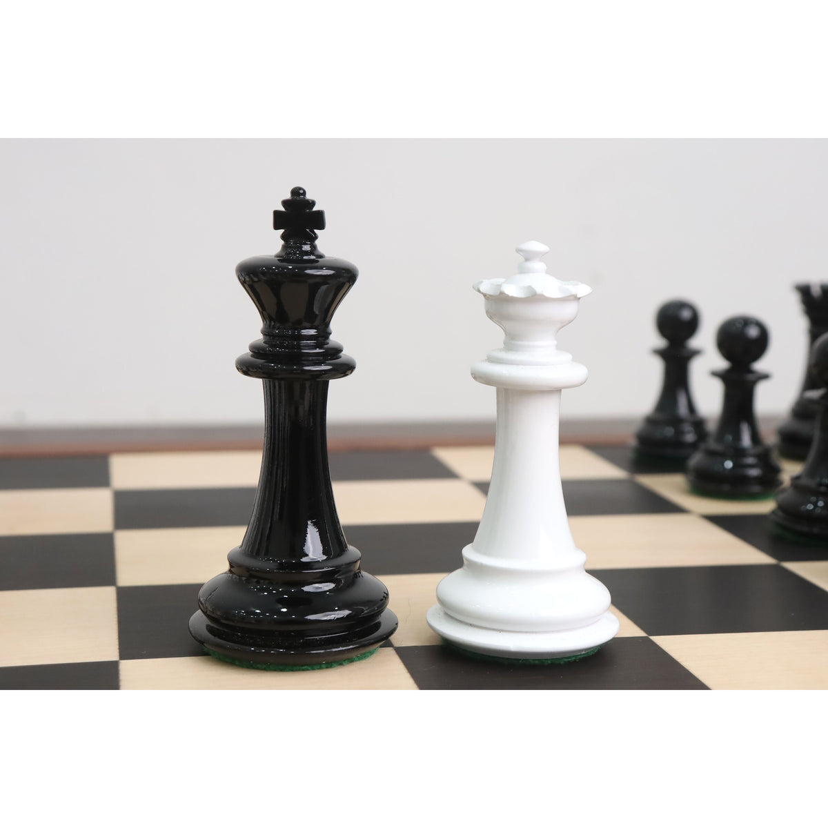Black King and white Queen texture painted Staunton chess pieces standing together on a wooden chessboard.