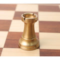 Close-up of a single antique brass Pro Staunton metal chess rook sitting on a chessboard.