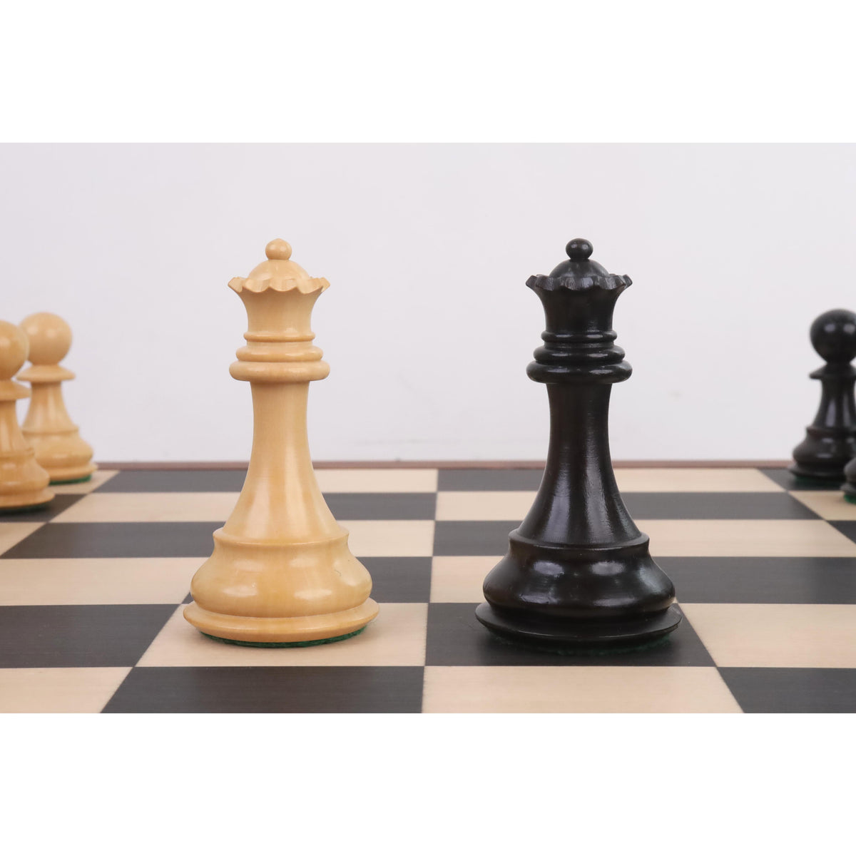 Light and dark queens from the 4" Fierce Knight Staunton chess set facing each other on a chessboard.