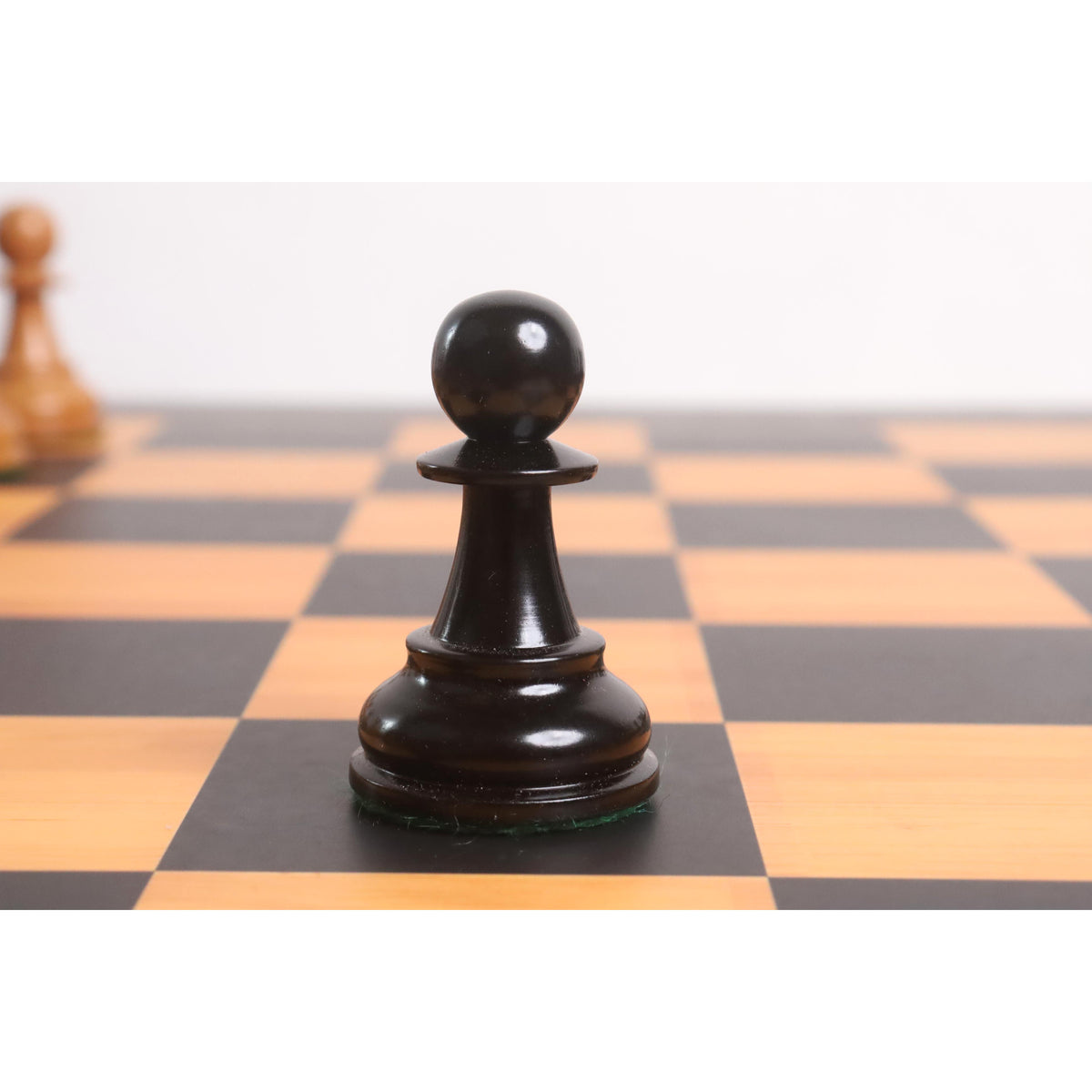 Single handcrafted black ebony Lessing Staunton pawn on wooden board.