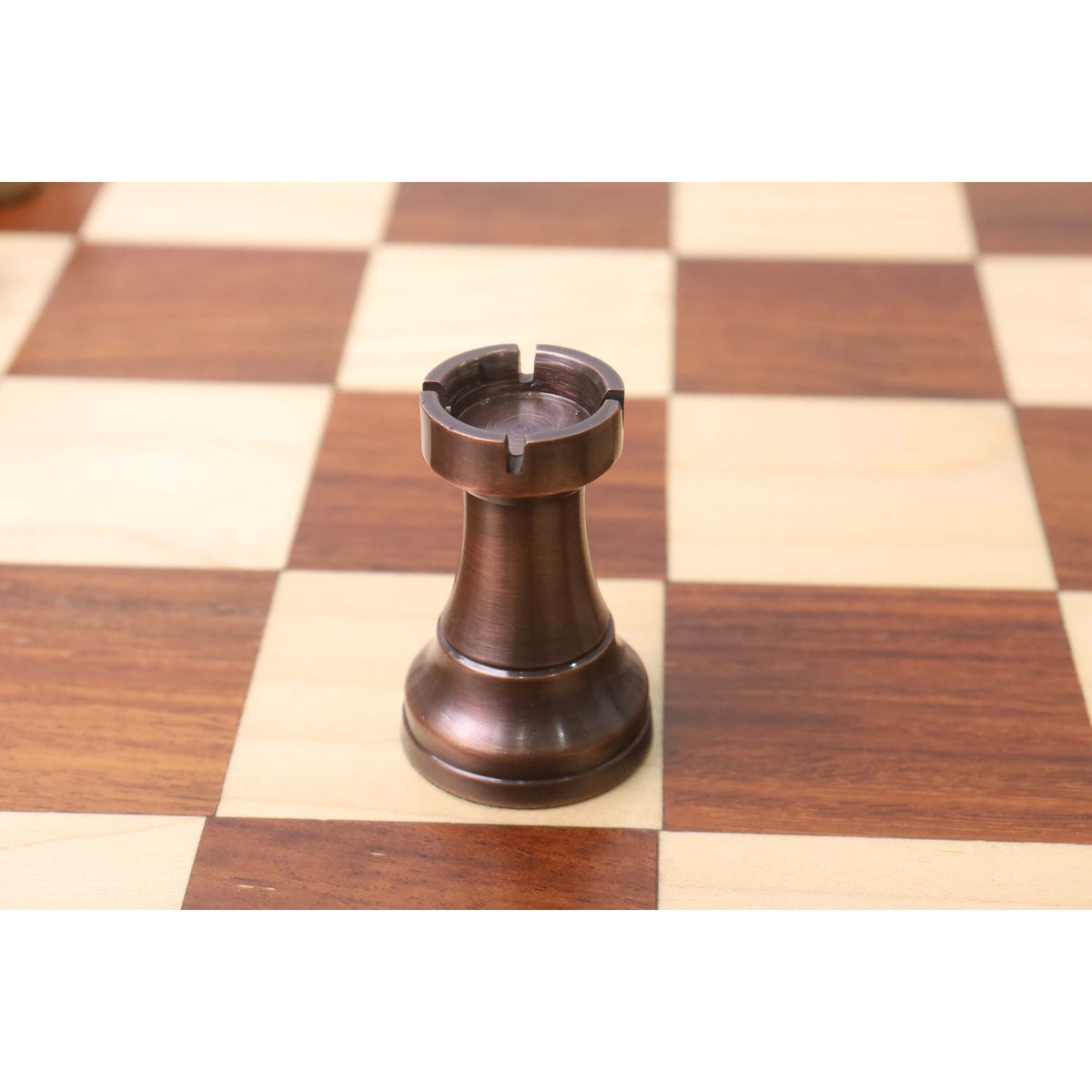 Close-up of a single copper Pro Staunton metal chess rook sitting on a chessboard.