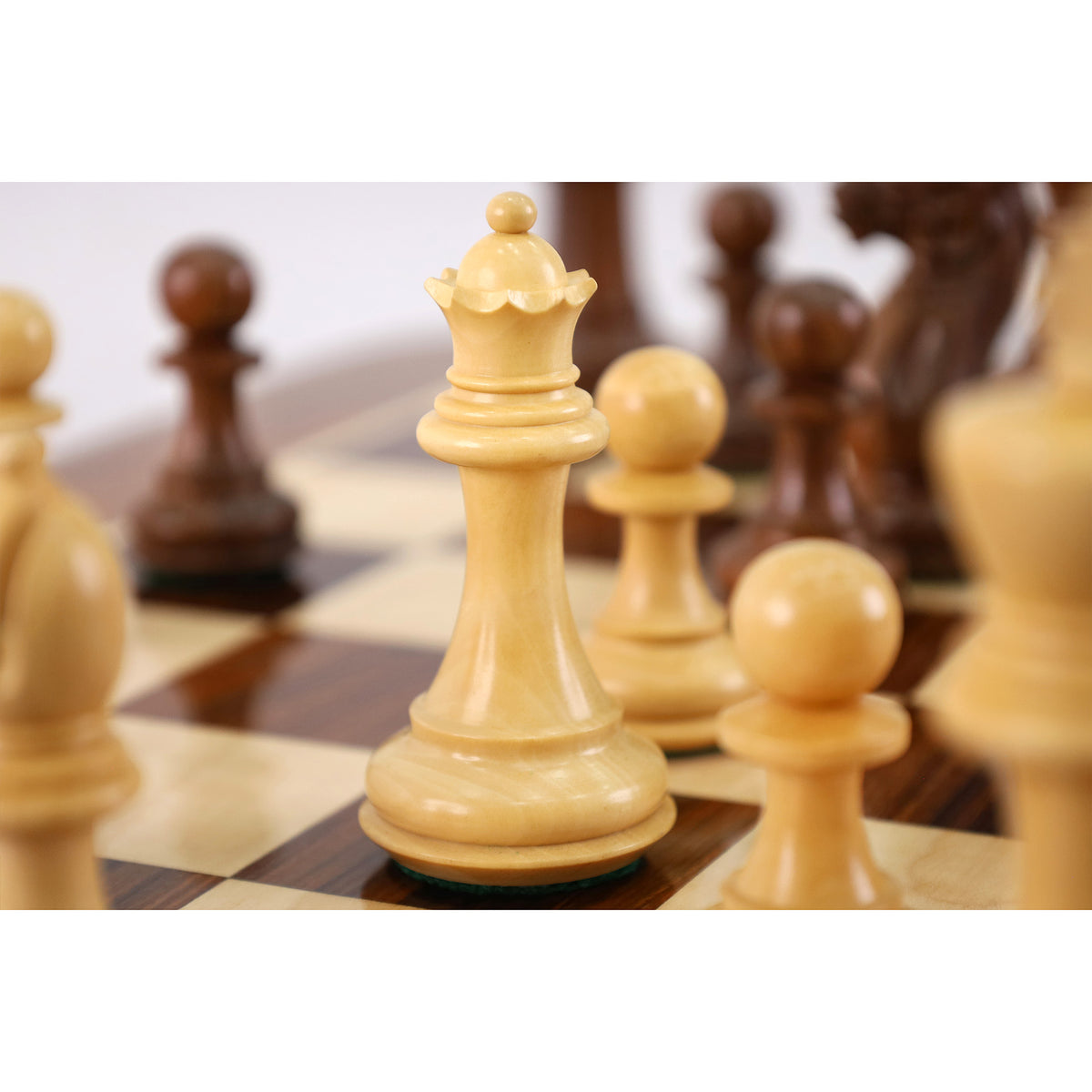 Close-up of a carved light boxwood queen chess piece on a rosewood board.