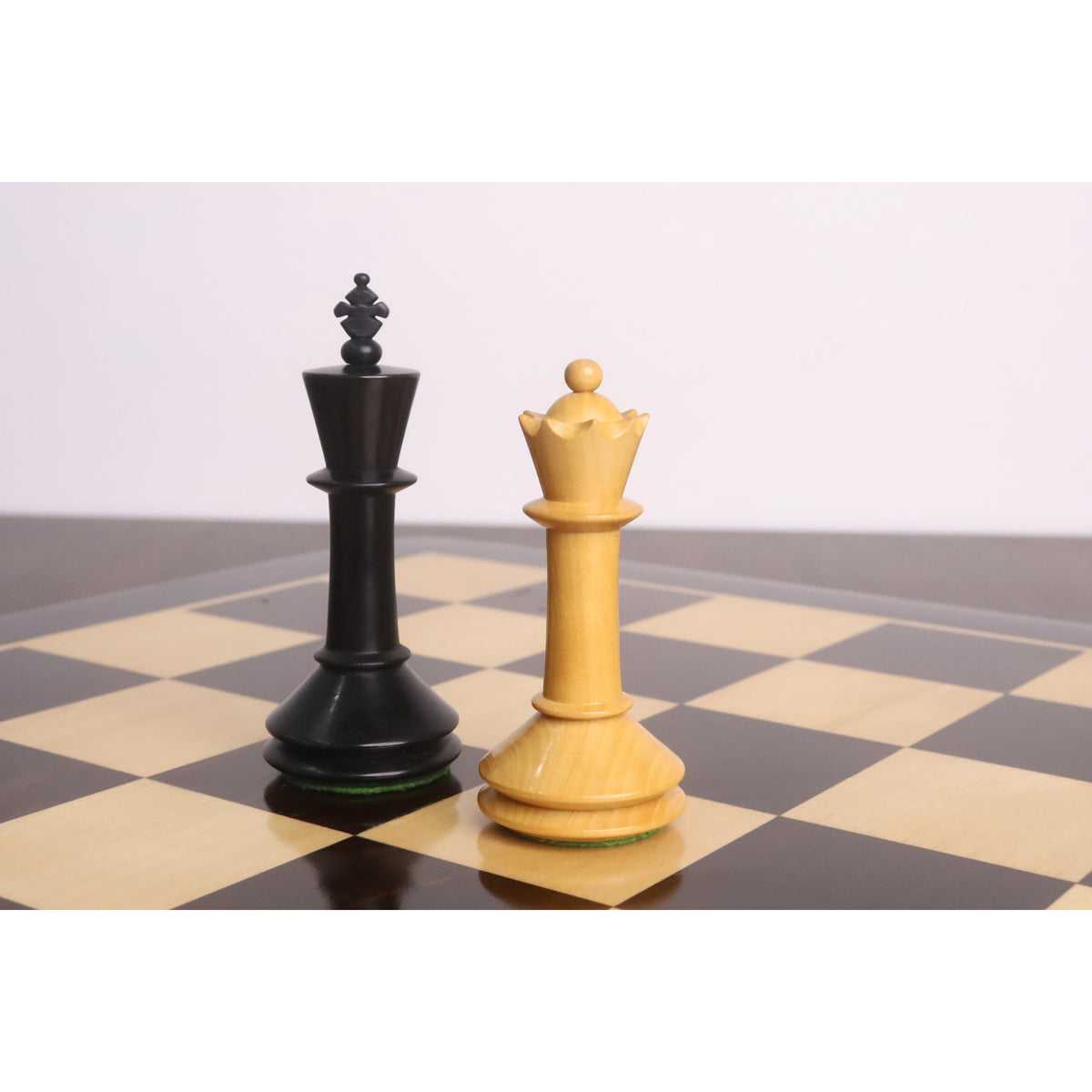 An ebonised dark king and a light boxwood queen from the Monolith miniature chess pieces on a wooden board.