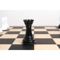 Close-up of a black texture painted Staunton Rook chess piece standing alone on a wooden chessboard.