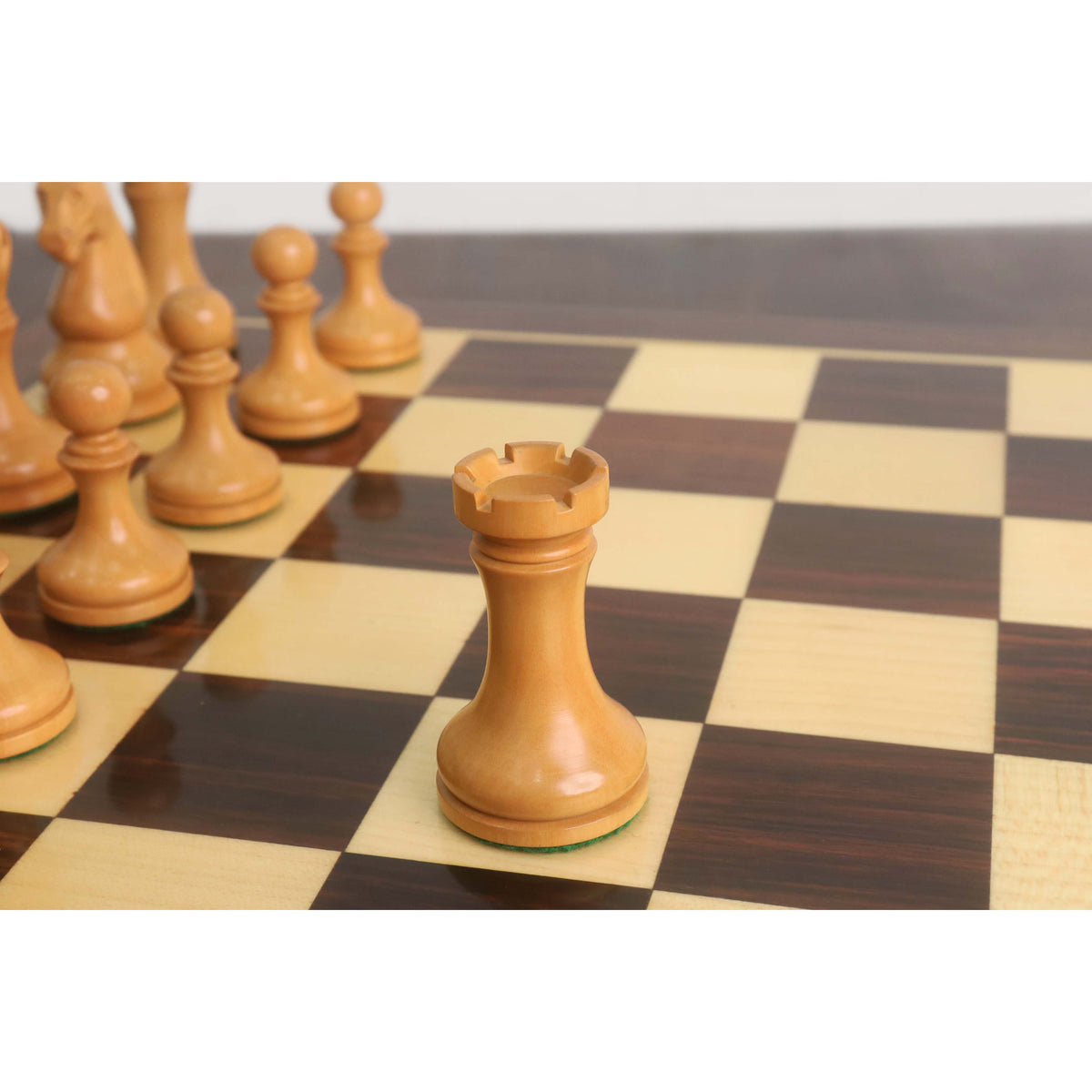 Close-up of the light antiqued boxwood rook from the Candidates Series minimalist chess set on a wooden chessboard.