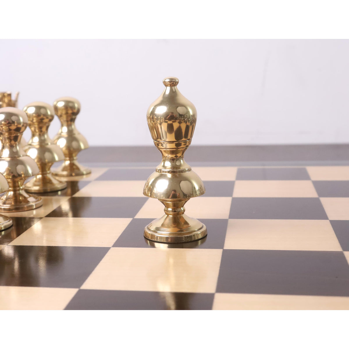Gold brass Victorian metal chess bishop standing on a glossy chessboard.