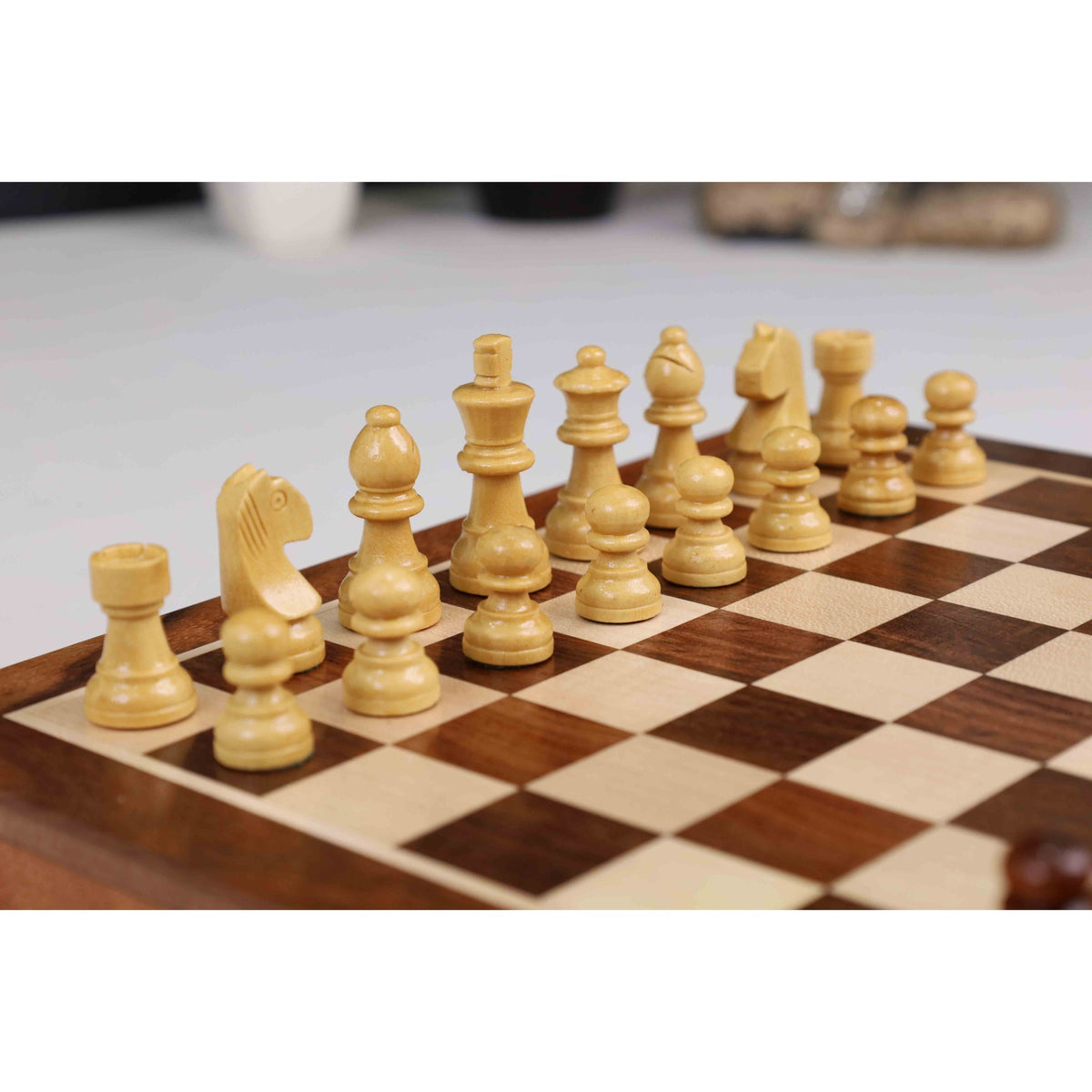 Light wooden magnetic chess pieces set up for play on a travel-sized rosewood board.