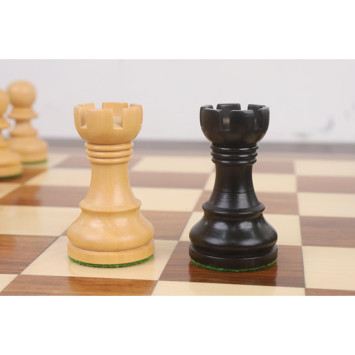 Light and dark ebonised boxwood Rooks from the Taj Mahal chess set side-by-side on a wooden board.