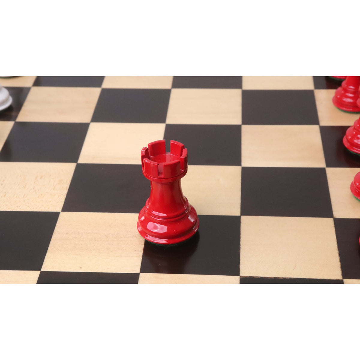 Glossy red painted wooden rook piece centered on a dark chess board square.