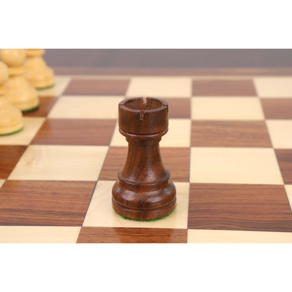 A detailed close-up of the Golden Rosewood Staunton chess rook, showcasing its precise castle-top crenelations on a wooden board.