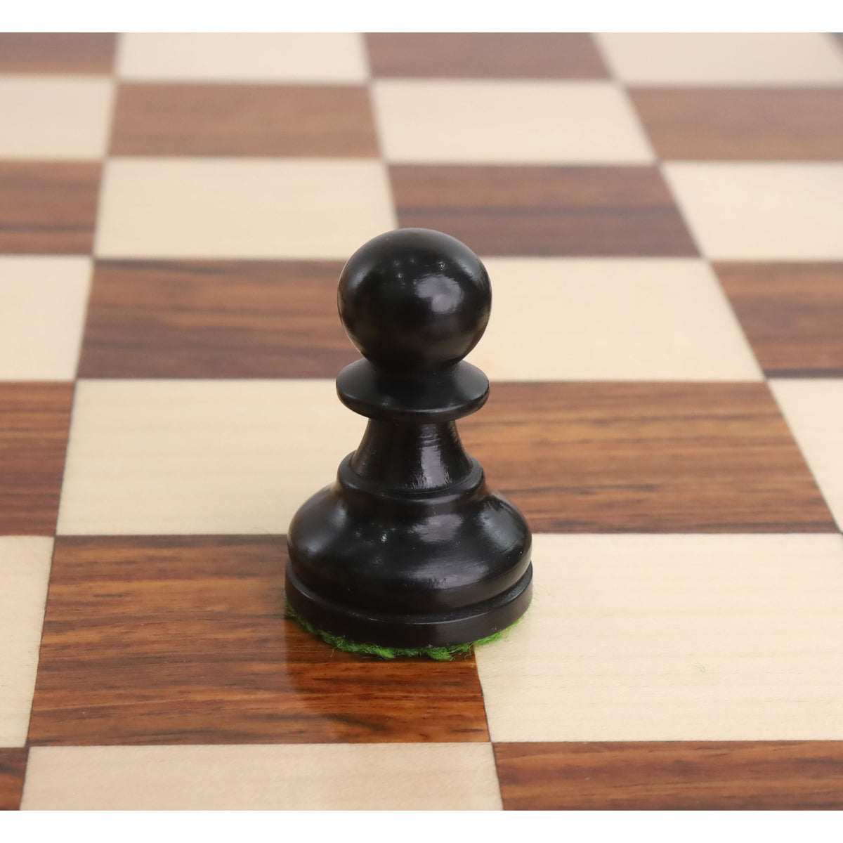 A single black Staunton chess pawn on a wooden board.