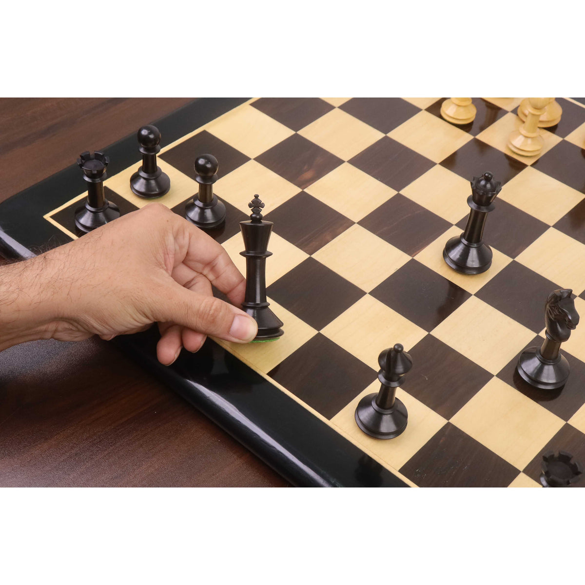 A player's hand moves the ebonised king across the chessboard during a game with the Monolith miniature set.