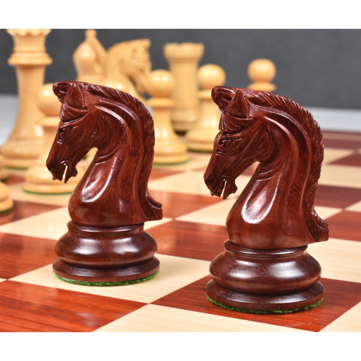 Close-up of intricately carved bud rosewood knight pieces on a wooden chess board.