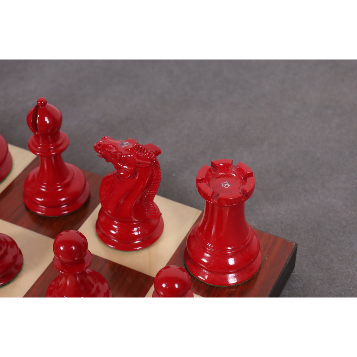 Angled close-up of red Staunton chess pieces positioned on a chessboard.