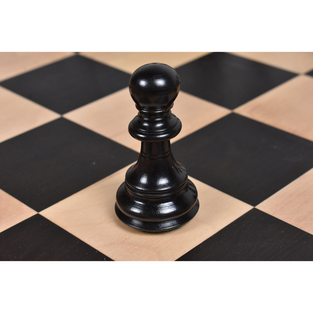 Natural ebony pawn piece from the 4.6 inch Prestige Luxury Staunton set on a wooden chessboard.