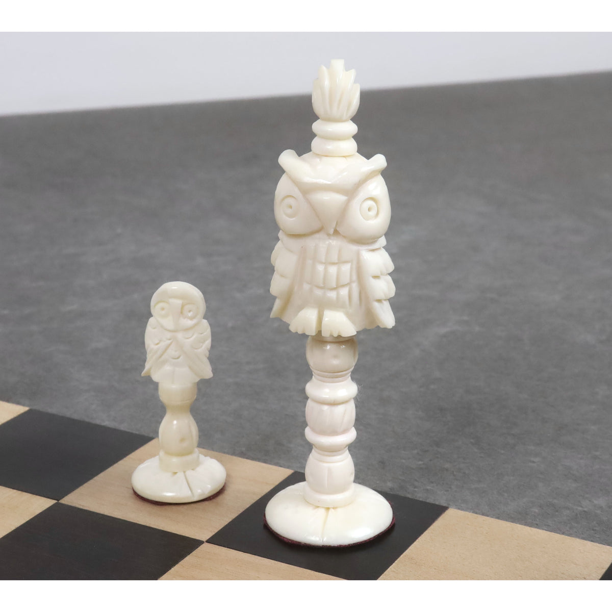 Beautifully carved white camel bone owl pawn and matching tall owl piece displayed on a wooden chessboard.