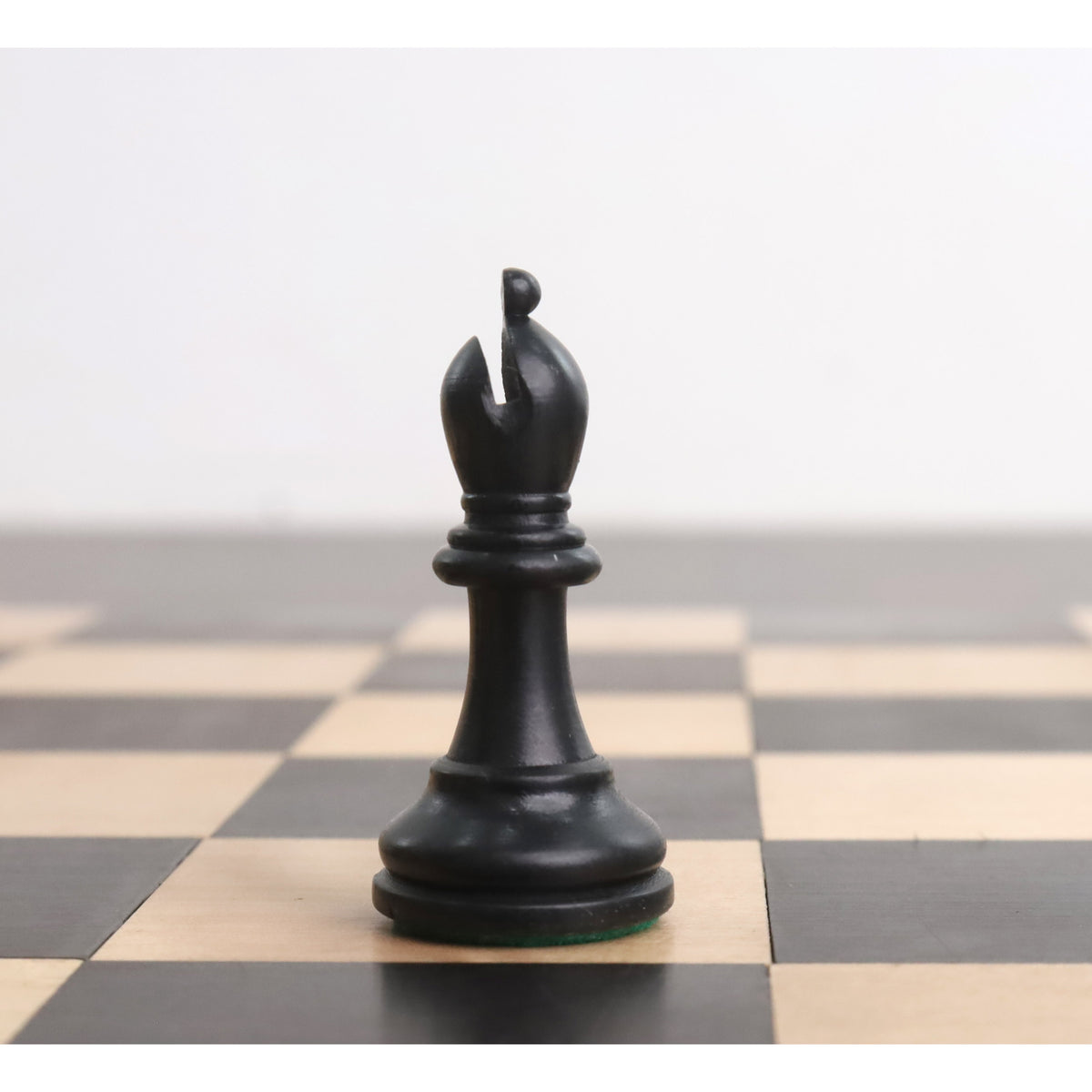 Single ebonised boxwood bishop piece centered on a wooden chess board square.