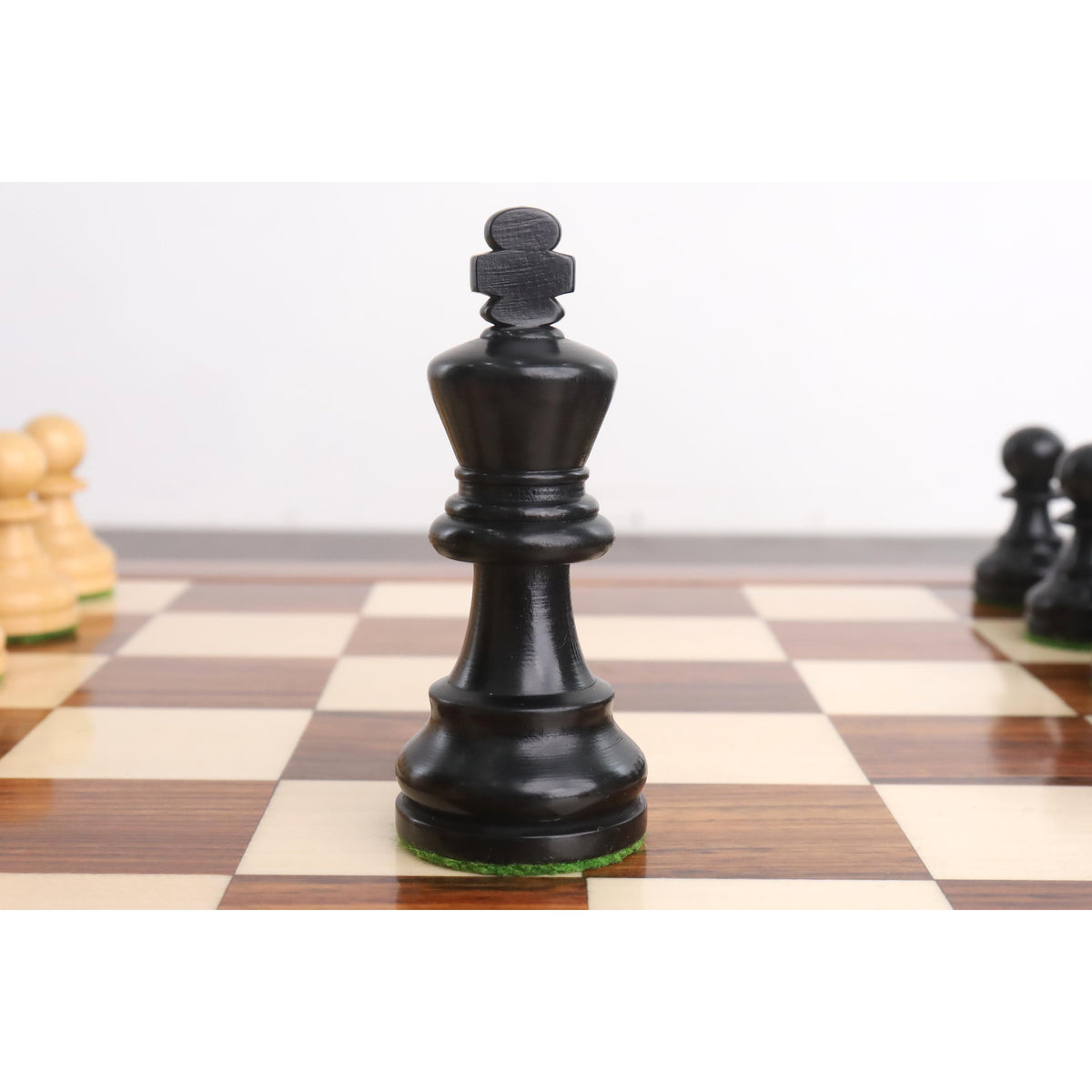 Black ebonised Staunton king chess piece centered on a wooden tournament chessboard.
