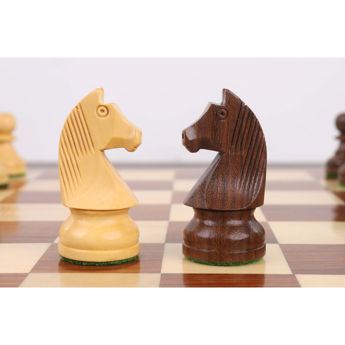 Close-up of boxwood and golden rosewood Staunton knights facing each other on a chessboard.