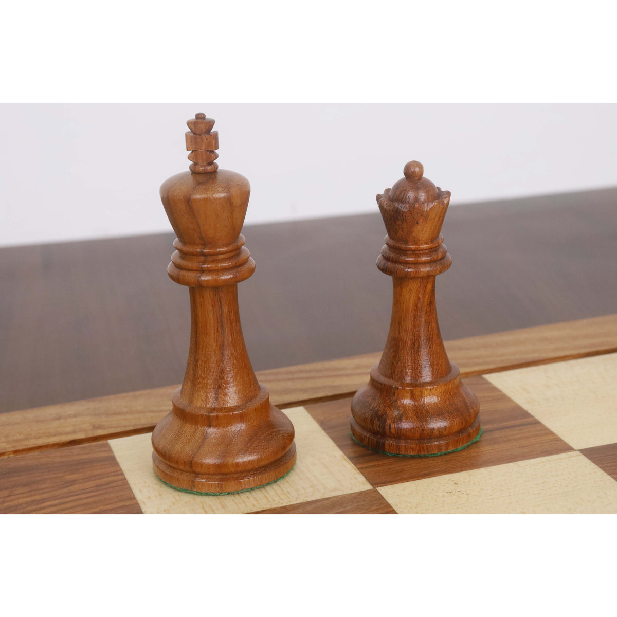 Dark Staunton king and queen chess pieces resting on a wooden board.
