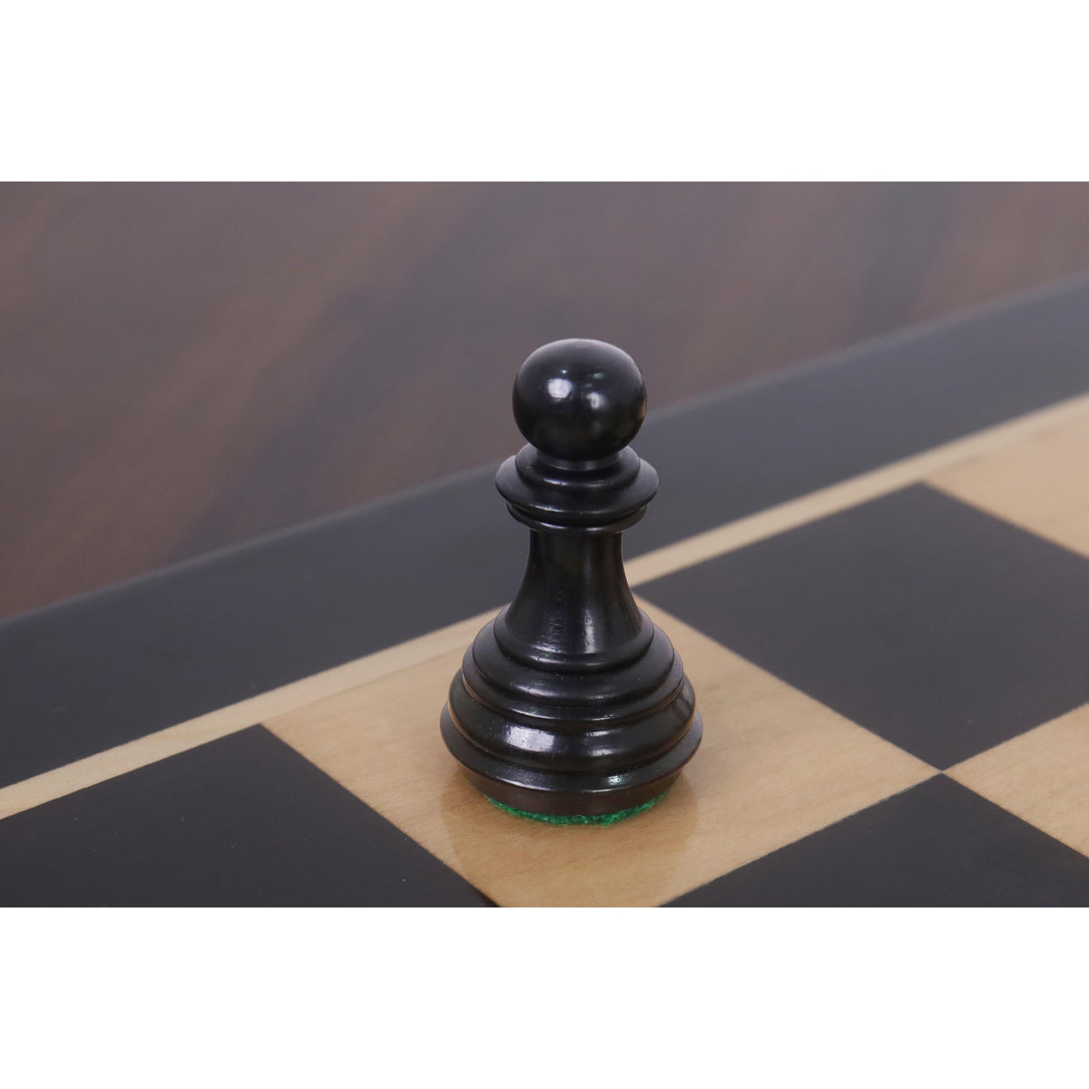 Close-up of a black ebony Imperial Staunton pawn standing on a maple square.