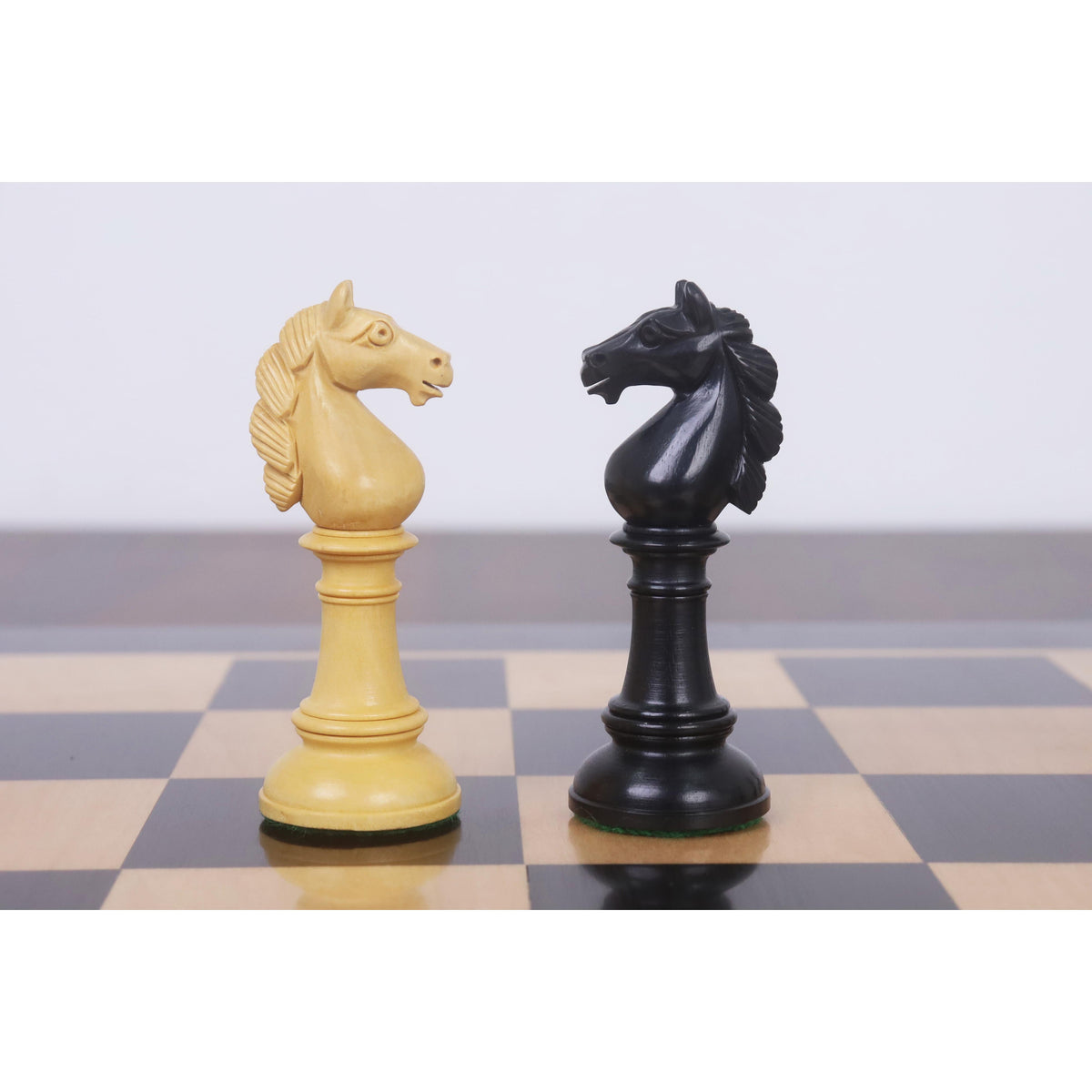 Hand-carved boxwood and ebony knights positioned face to face on a wooden chessboard.