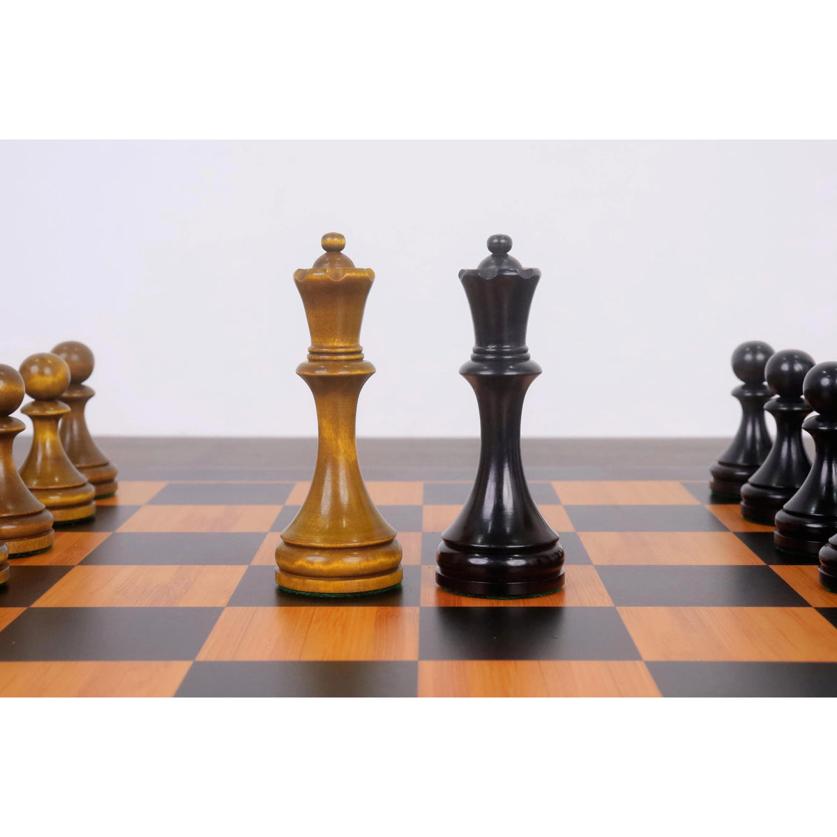 Soviet style chess Queens in distressed antiqued boxwood and ebonised boxwood on a checkered board.
