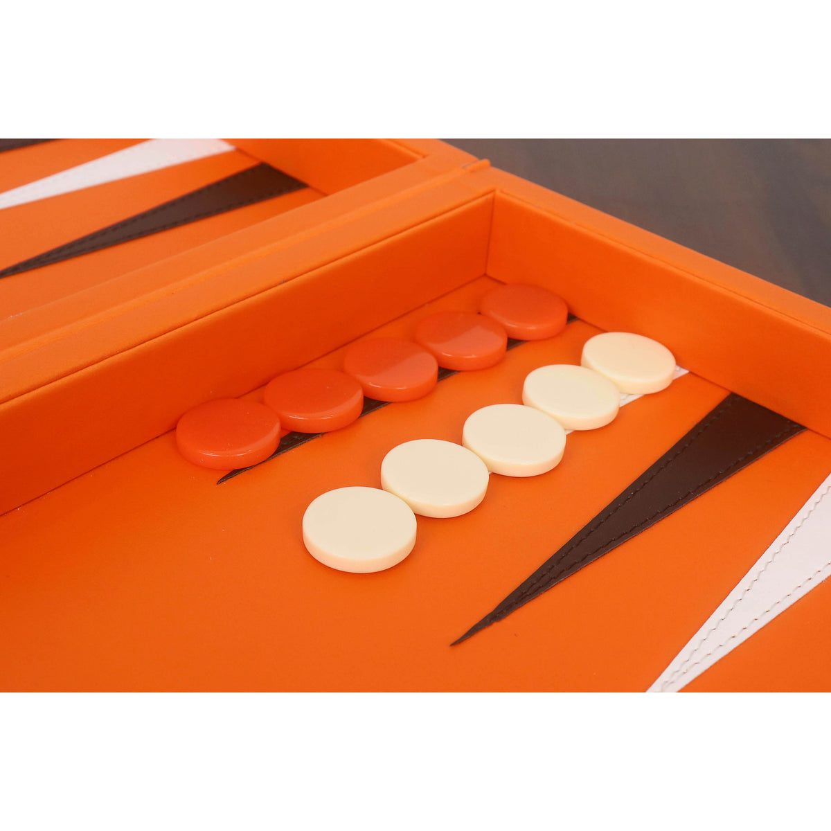 Close-up of cream and orange backgammon checkers on black and white stitched leatherette triangular pips.