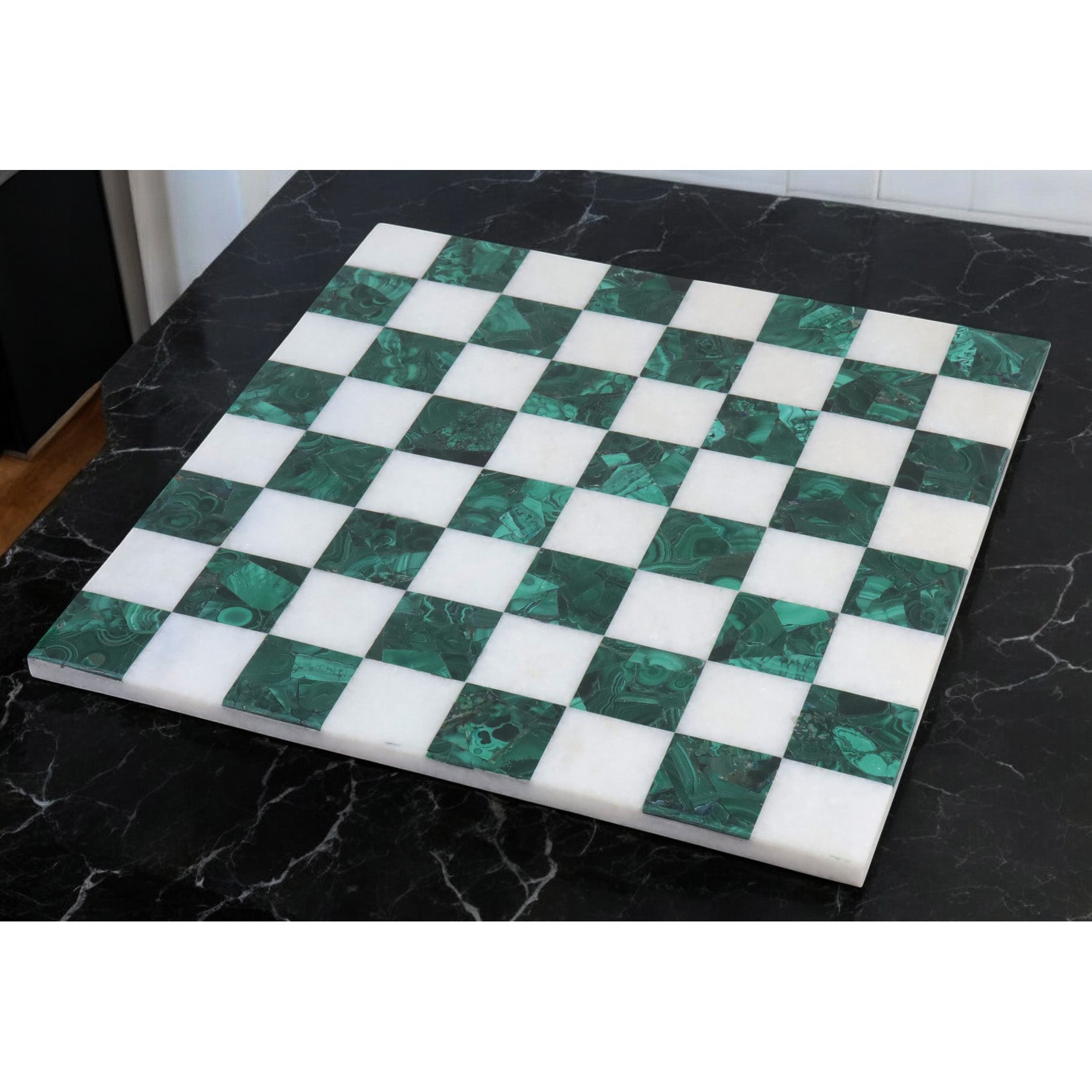 Premium green malachite and white stone chess board displayed on a black marble tabletop.
