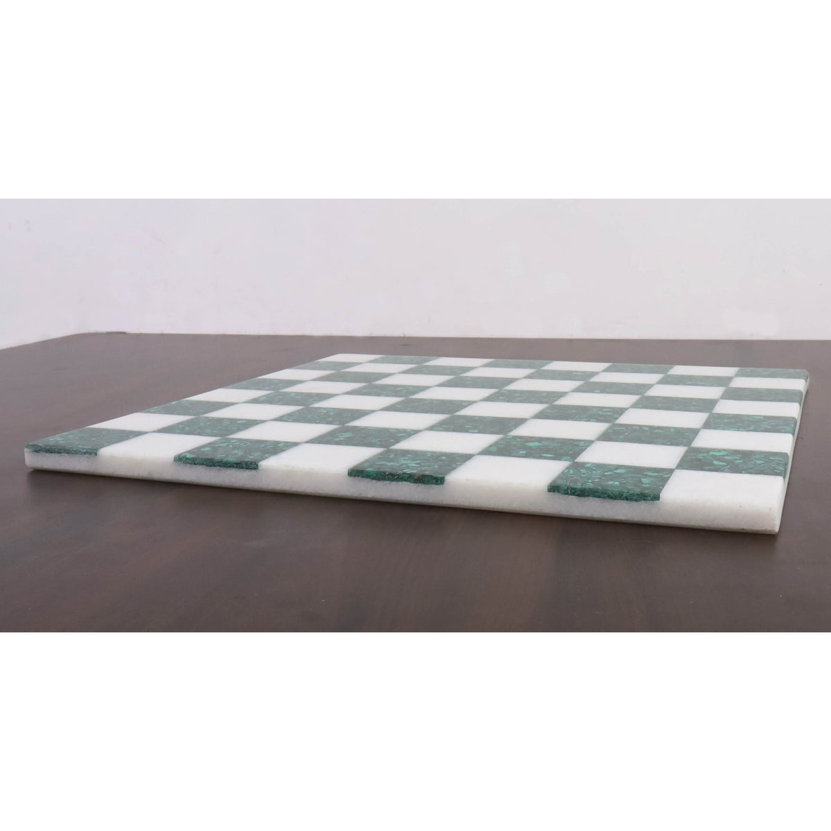 Low-angle side profile of a slim borderless malachite stone chess board on a dark surface.