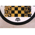 Top-down view of a minimalist chess board featuring a black crown emblem and polished metal pieces.