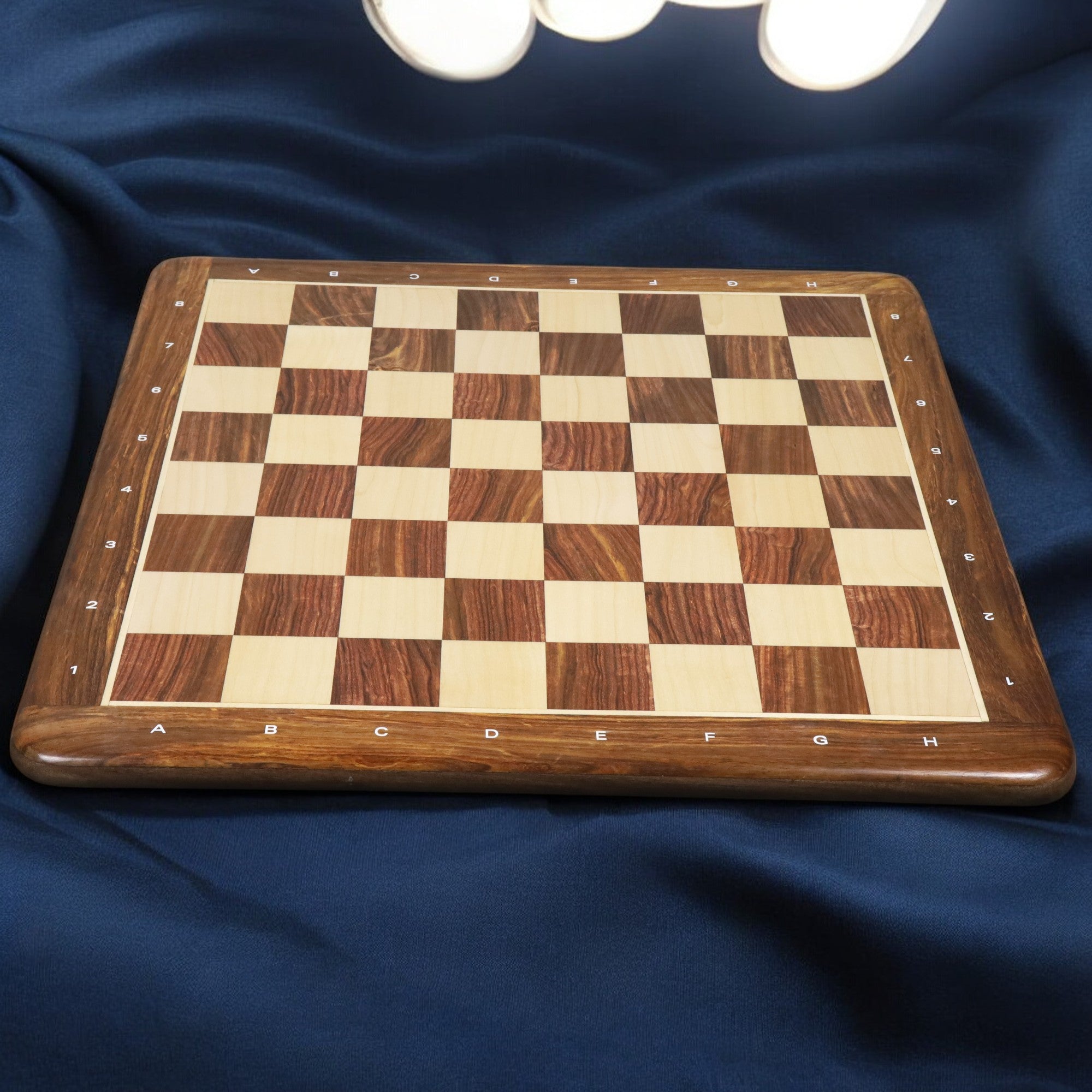 Full view of a 19 inch wooden chess board with maple and rosewood squares on a blue draped background.