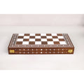 Closed folding wooden chess board featuring ornate white engraved border patterns and secure brass clasps.