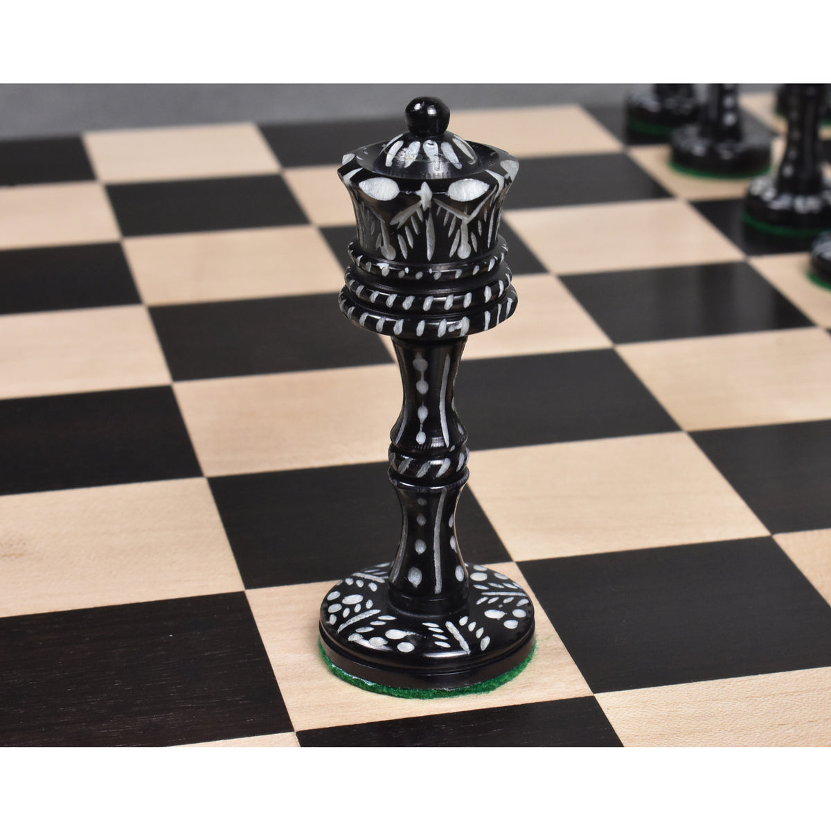 Intricately carved black camel bone Victorian era pre-Staunton queen piece placed on a wooden chessboard.