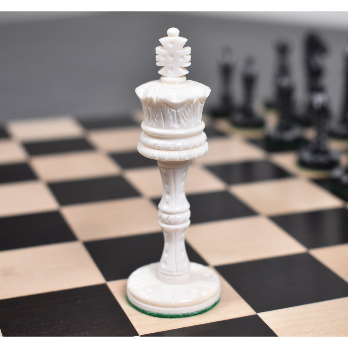 White camel bone Victorian era pre-Staunton king piece featuring intricate carvings on a wooden chess board.