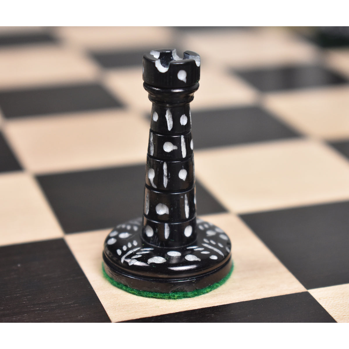 Black dyed camel bone Victorian era pre-Staunton rook piece displaying detailed circular carvings on a chessboard.