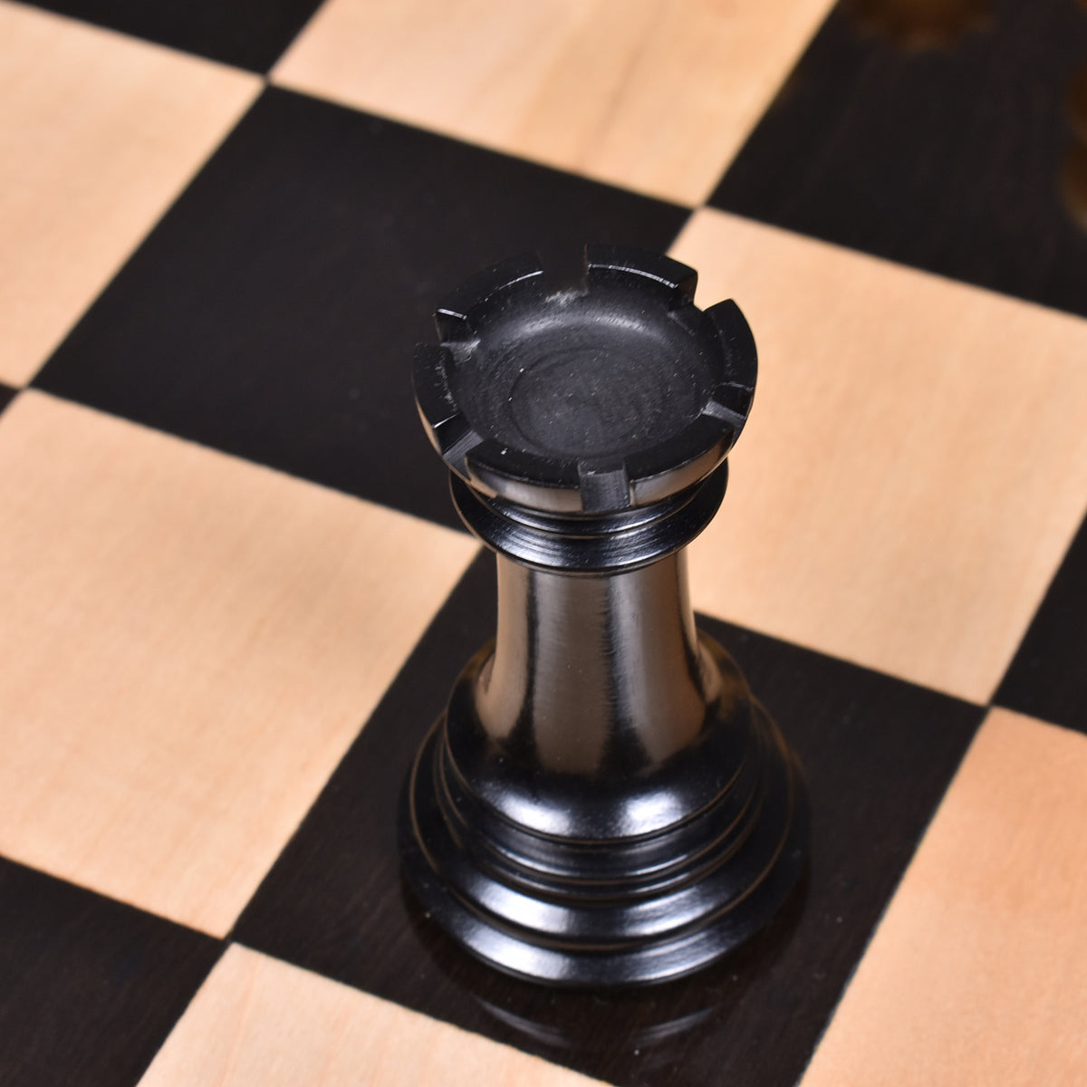 Black ebony wood Mogul Staunton rook piece on a chessboard.