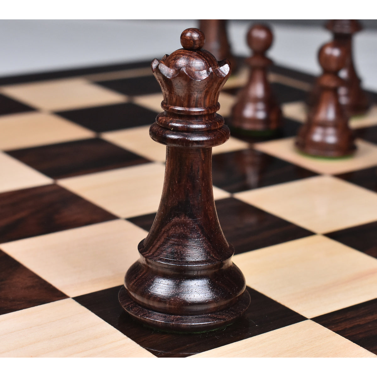 Dark rosewood Majestic Staunton queen on a wooden board, featuring a crisp crown detail against a blurred background.