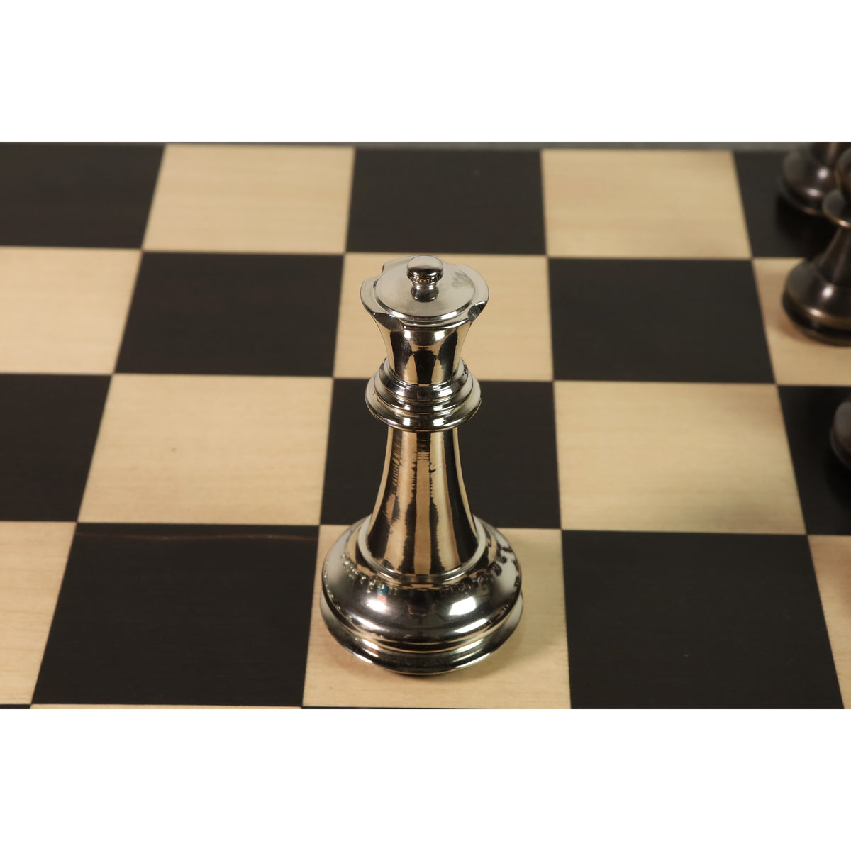 Polished silver brass metal luxury chess piece Queen shown from an overhead perspective on a checkered board.