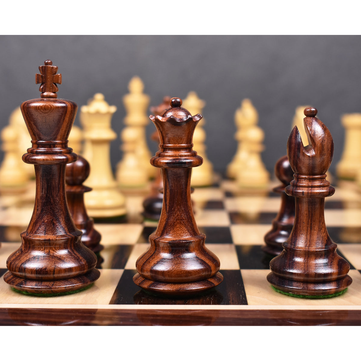 Dark rosewood king, queen, and bishop from the 3.9" Craftsman Staunton chess set with blurred light pieces behind.