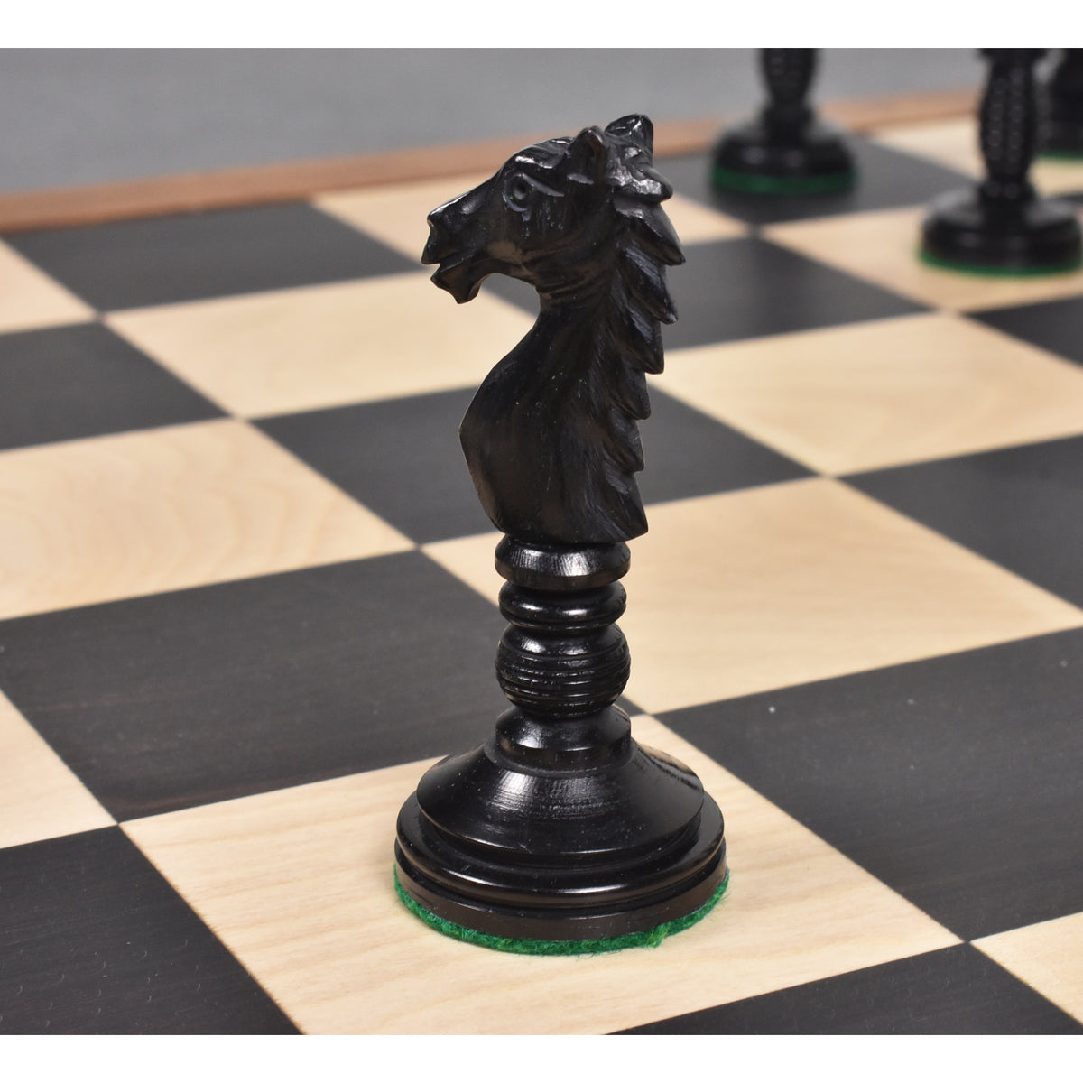 Profile of a black Minaret series hand-carved camel bone knight piece on a checkered chess board.