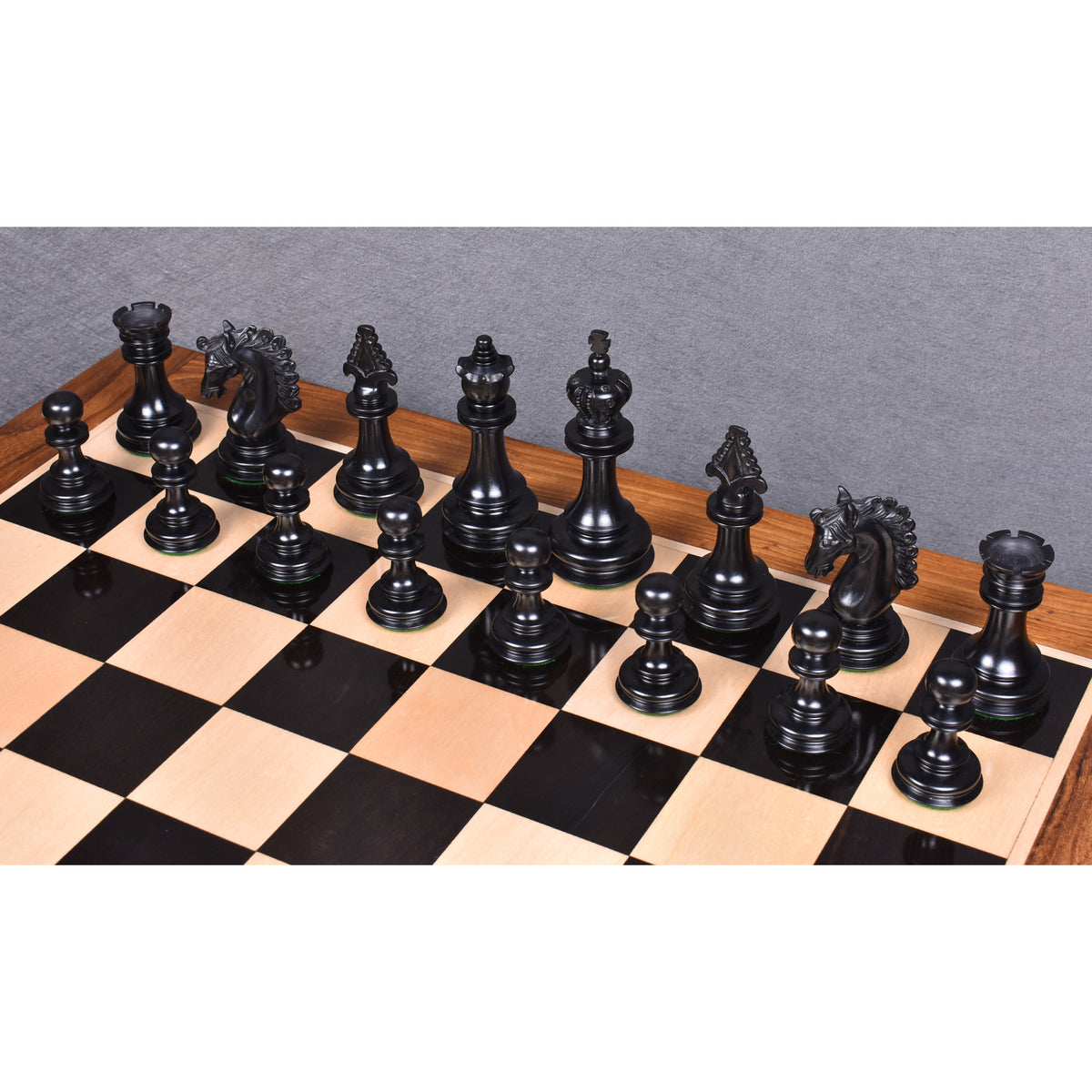 Full set of triple-weighted ebony wood chess pieces standing in formation on a board.