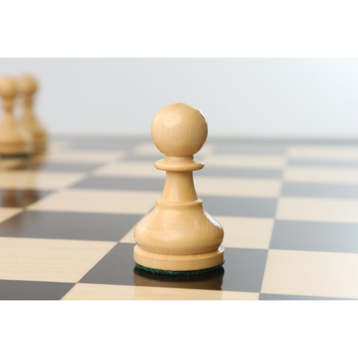 Single natural boxwood pawn piece highlighted on a glossy tournament chessboard.